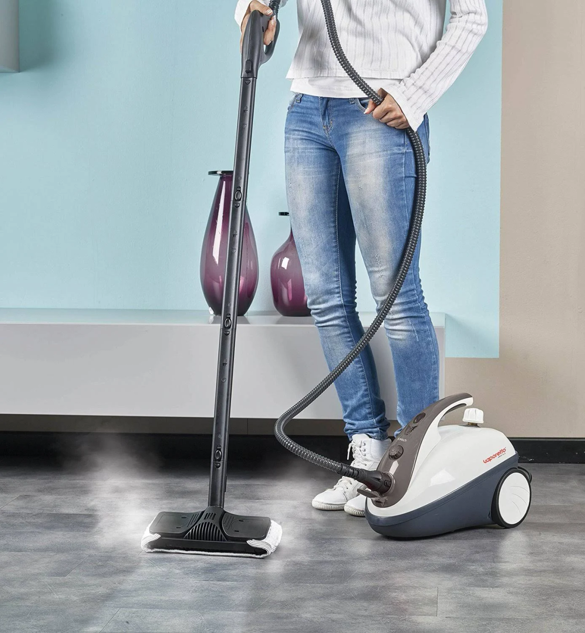 Osoba czyszcząca podłogę parownicą. Niebieska ściana i biała szafka w tle.