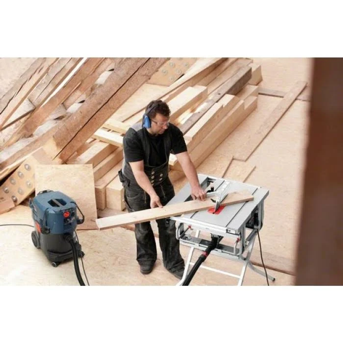 Un hombre usando una sierra de mesa. Una aspiradora junto a él en un taller.