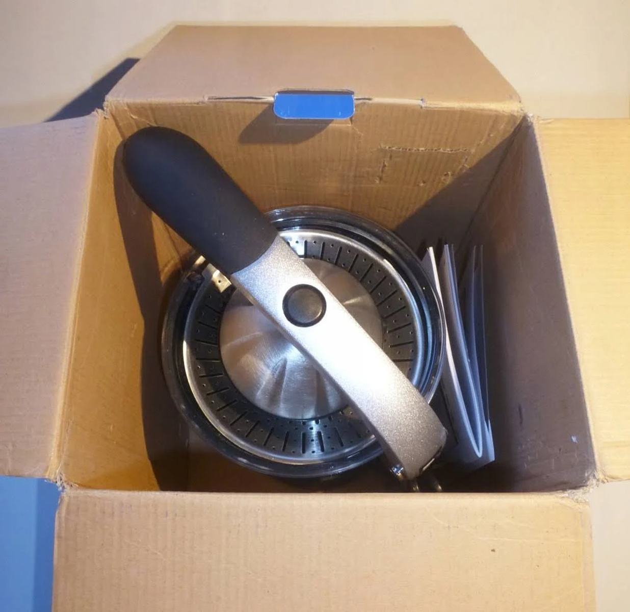 Caja de cartón abierta con una exprimidora dentro, piezas visibles, vista superior.