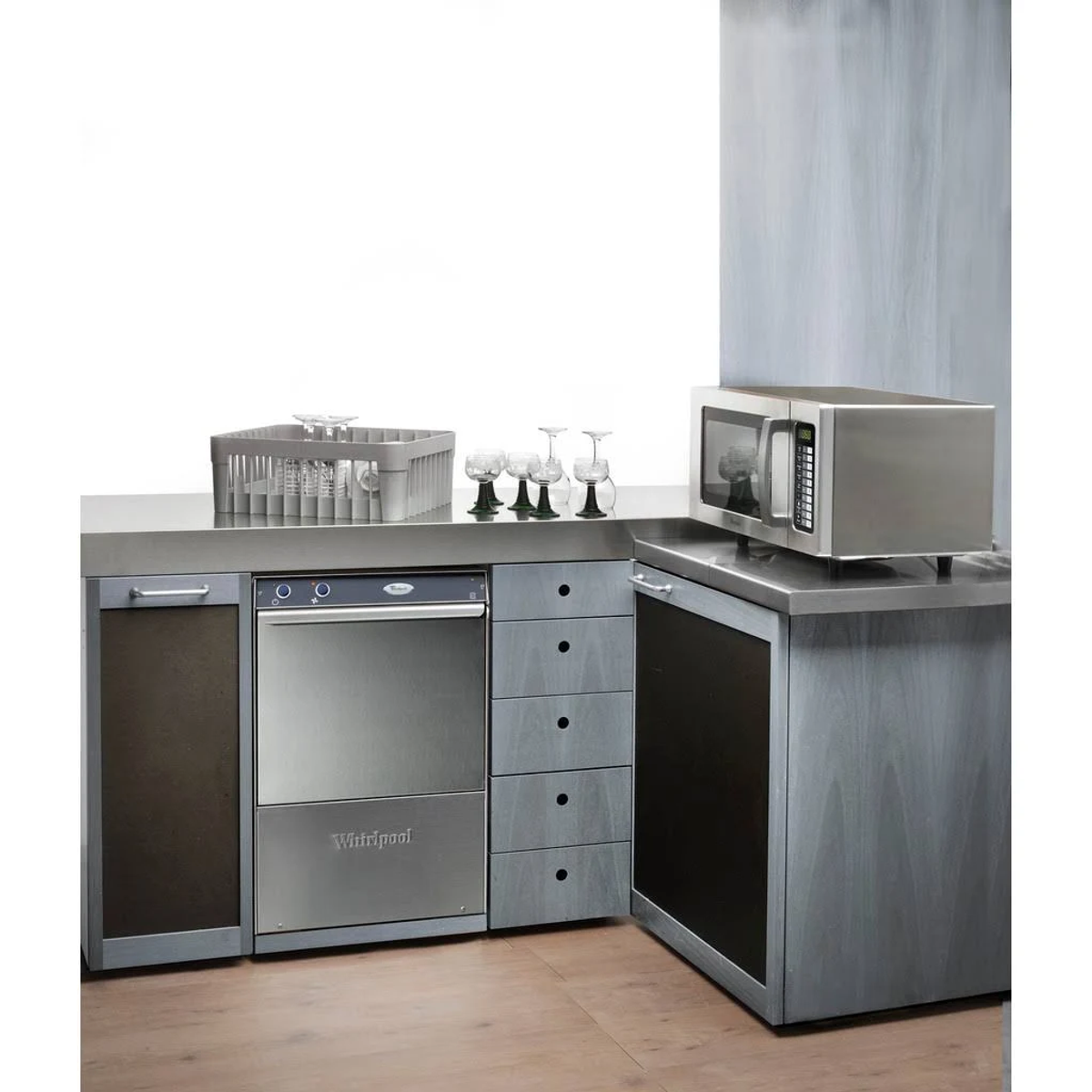 Cocina comercial con lavavajillas, microondas y armarios de acero inoxidable, todo en tonos grises.