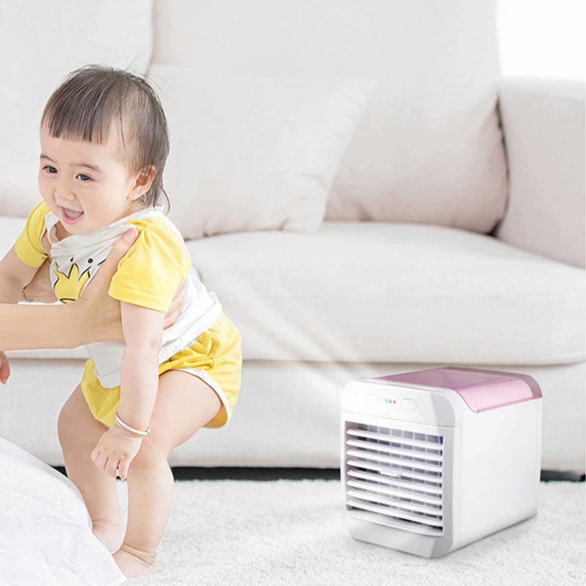Ein Baby und eine Frau neben einer weißen Couch. Ein kleiner weißer und rosa Luftkühler ist in der Nähe.