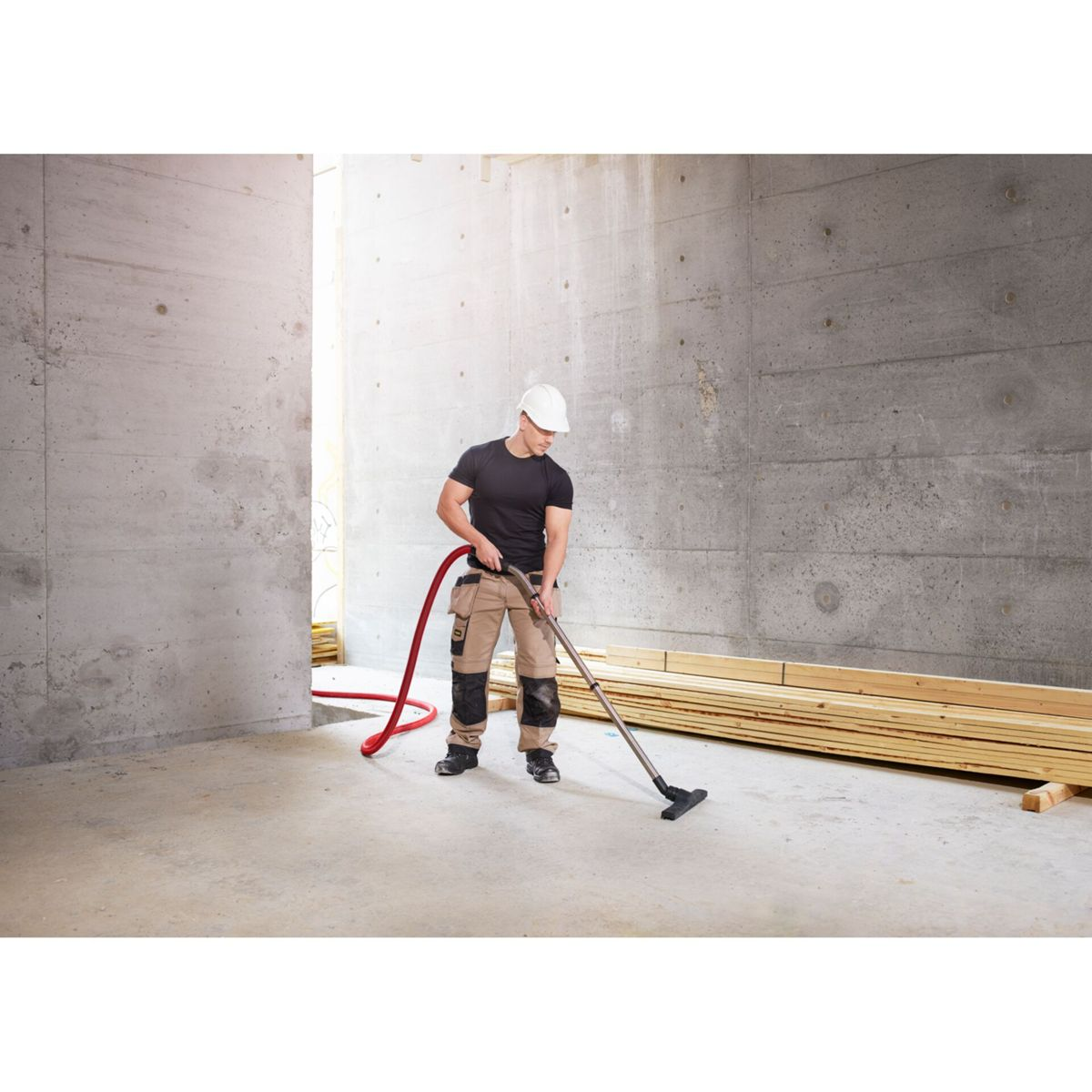 Un operaio edile aspira un pavimento in cemento in un cantiere, indossando dispositivi di sicurezza.