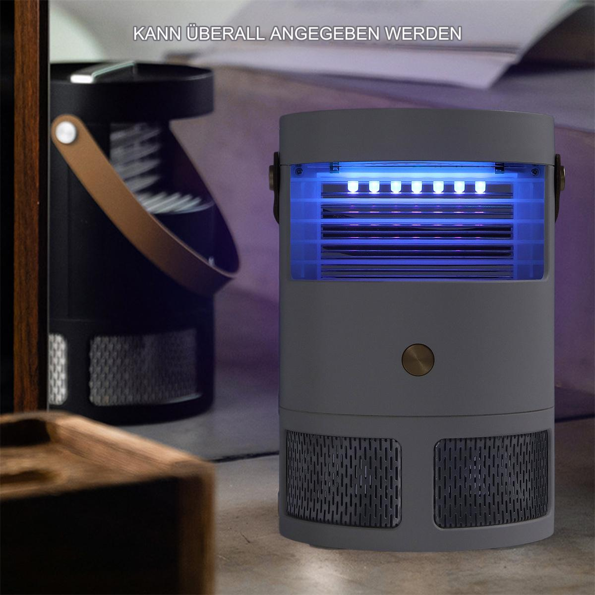 Ein grauer Mückenvernichter steht auf einem Tisch. Im Hintergrund steht eine dunkle Lampe.