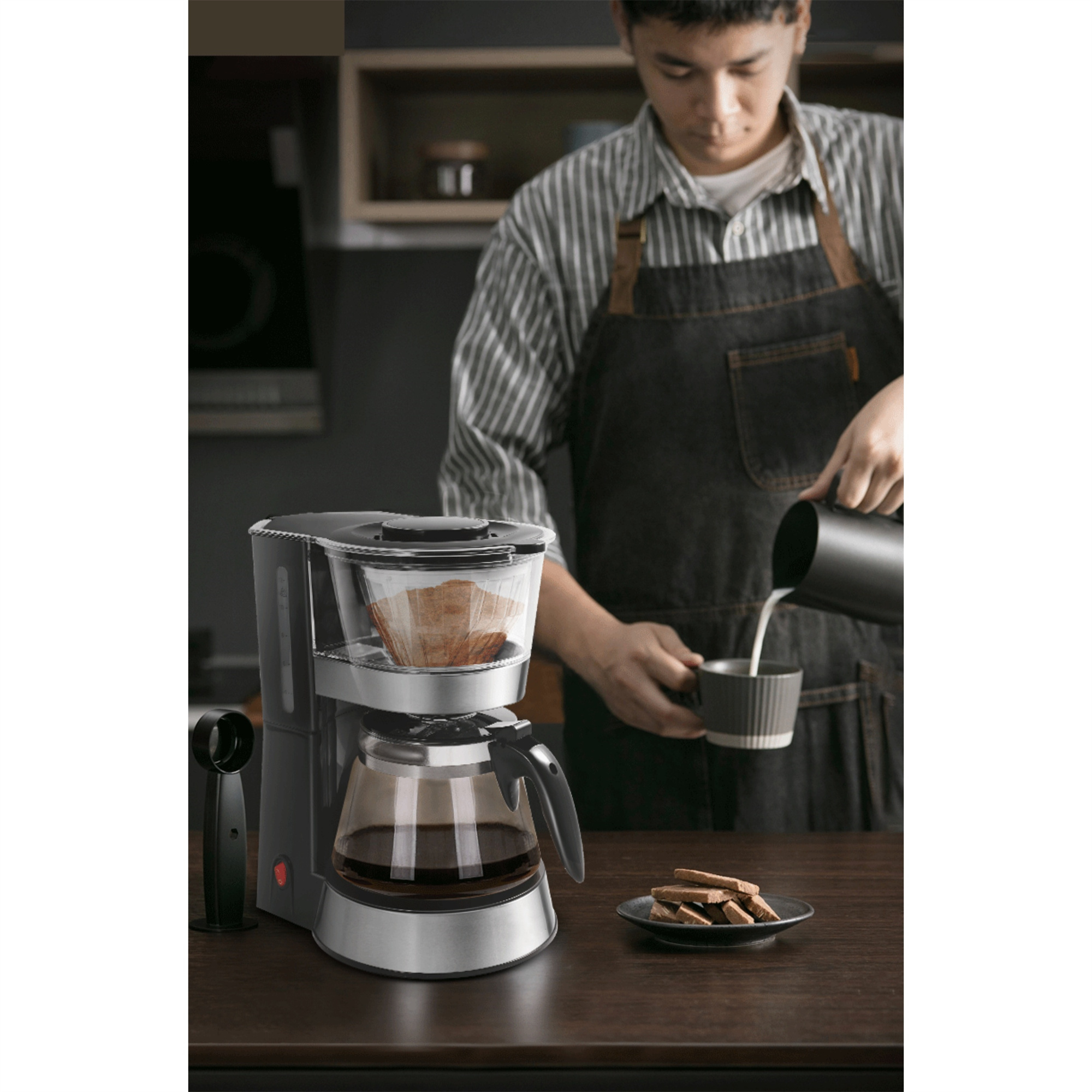 Eine Person gießt Milch in eine Tasse, in der Nähe einer Kaffeemaschine und Keksen.