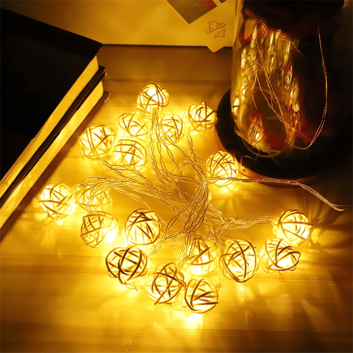 Eine Lichterkette mit leuchtenden Kugeln auf einem Tisch mit Buch und Glas.