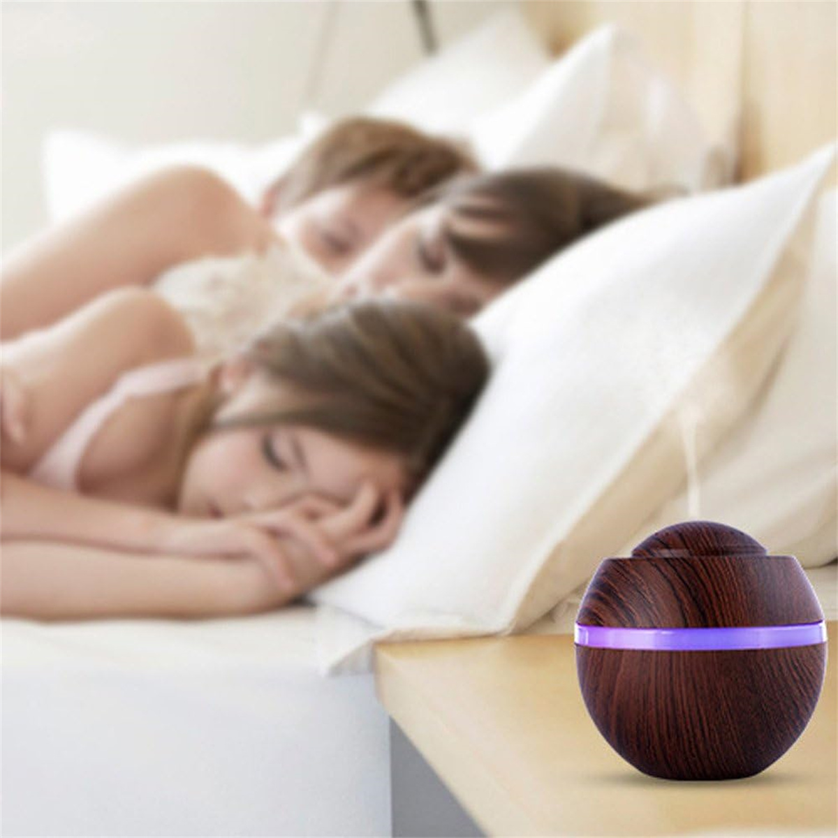 Ein hölzerner ätherischer Öldiffusor auf einem Nachttisch, mit drei Personen, die im verschwommenen Hintergrund schlafen.