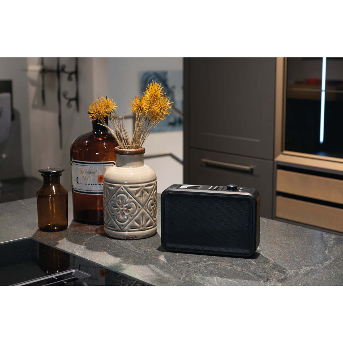 Czarny głośnik przenośny z brązowymi butelkami i żółtymi kwiatami.