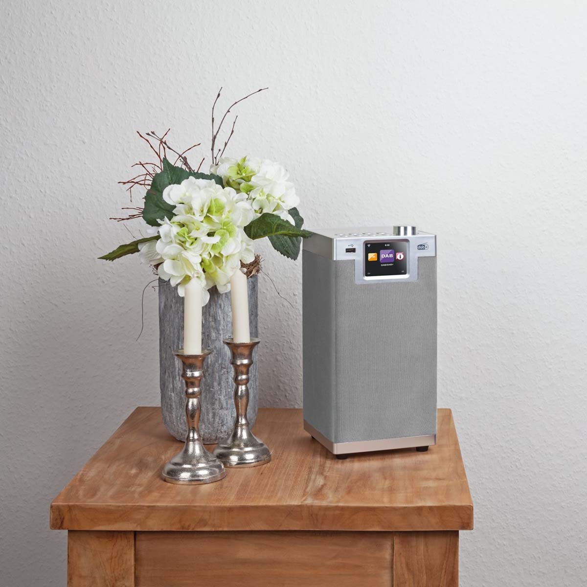 Radio on a wooden table with flowers and candlesticks.