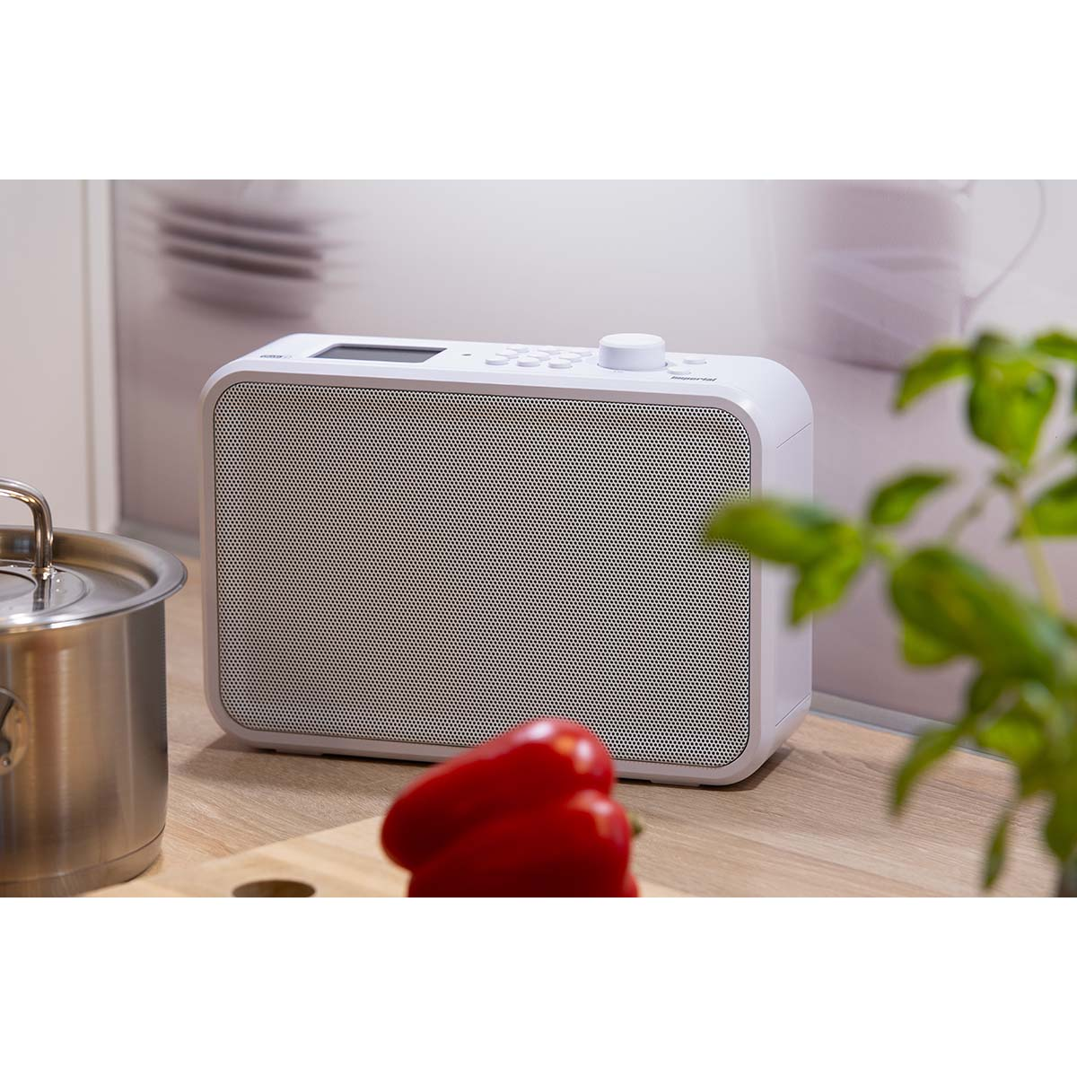 Białe radio z głośnikiem z siatki, czerwoną papryką i garnkiem na drewnianej powierzchni.