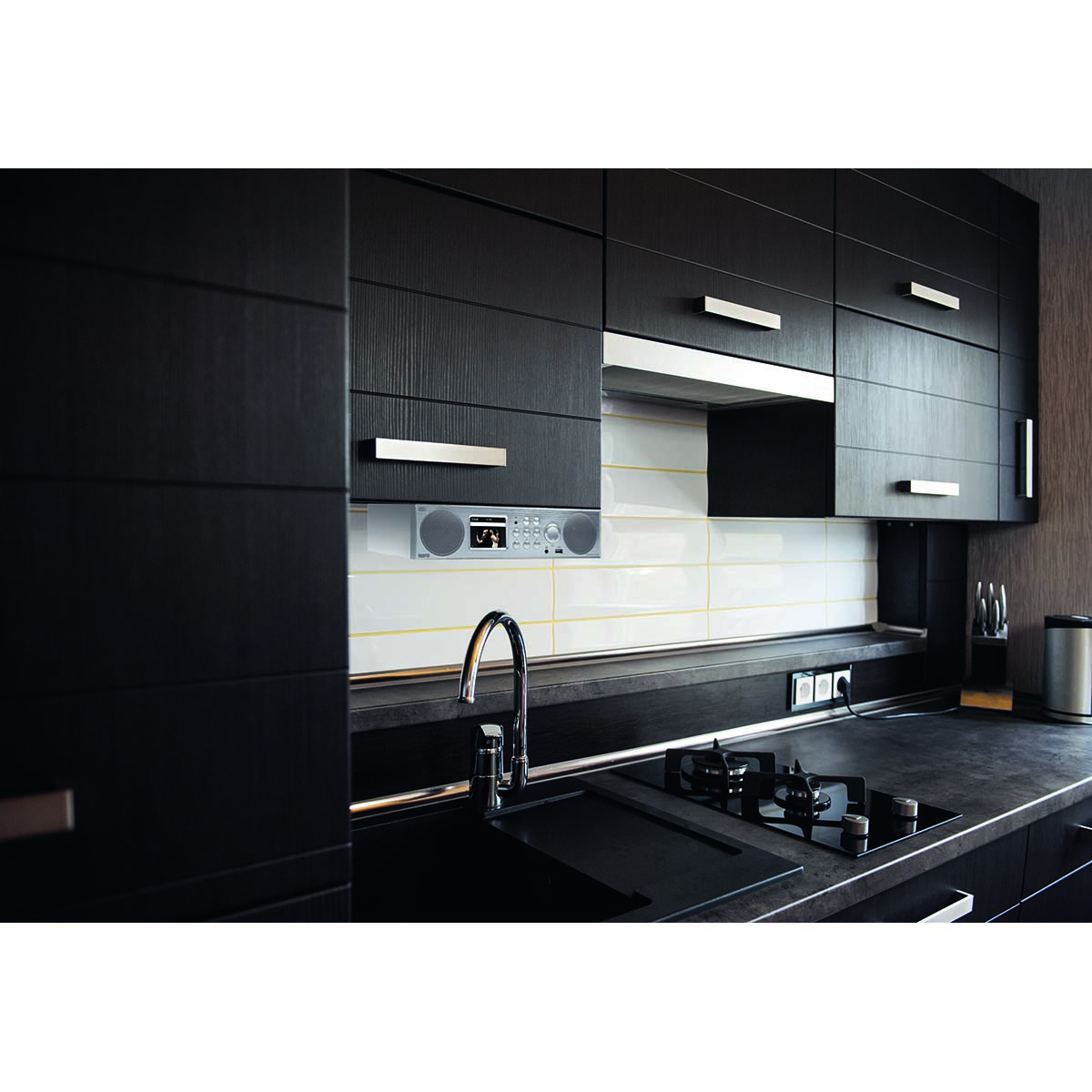 Cocina con gabinetes negros, fregadero y radio. La estufa está en la encimera.