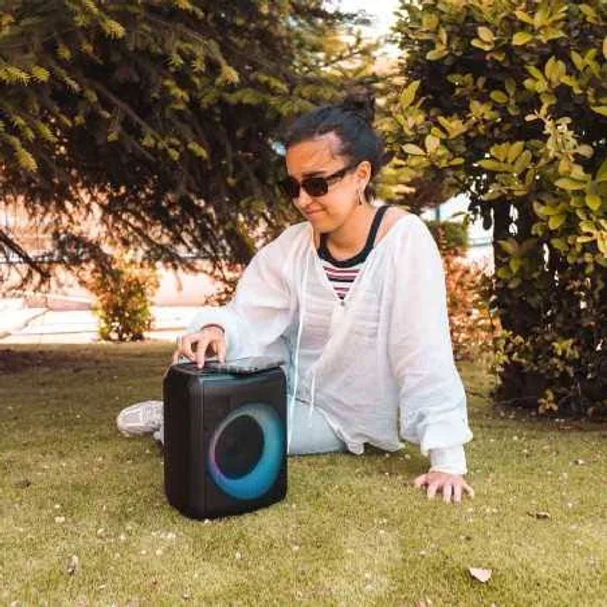 Una mujer sentada en la hierba opera un altavoz portátil negro.