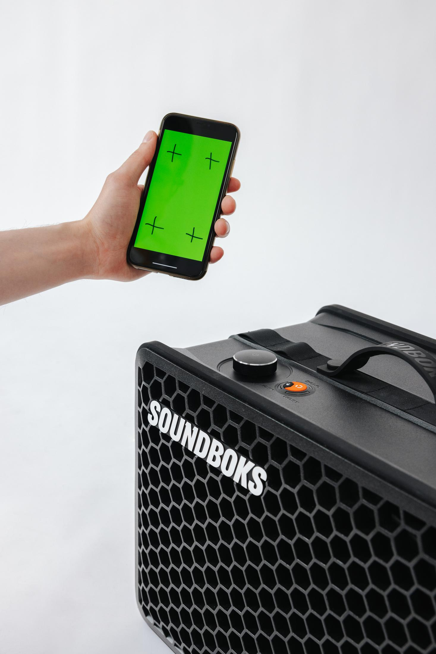 Eine Hand hält ein Telefon mit grünem Bildschirm in der Nähe eines schwarzen SOUNDBOKS-Lautsprechers.