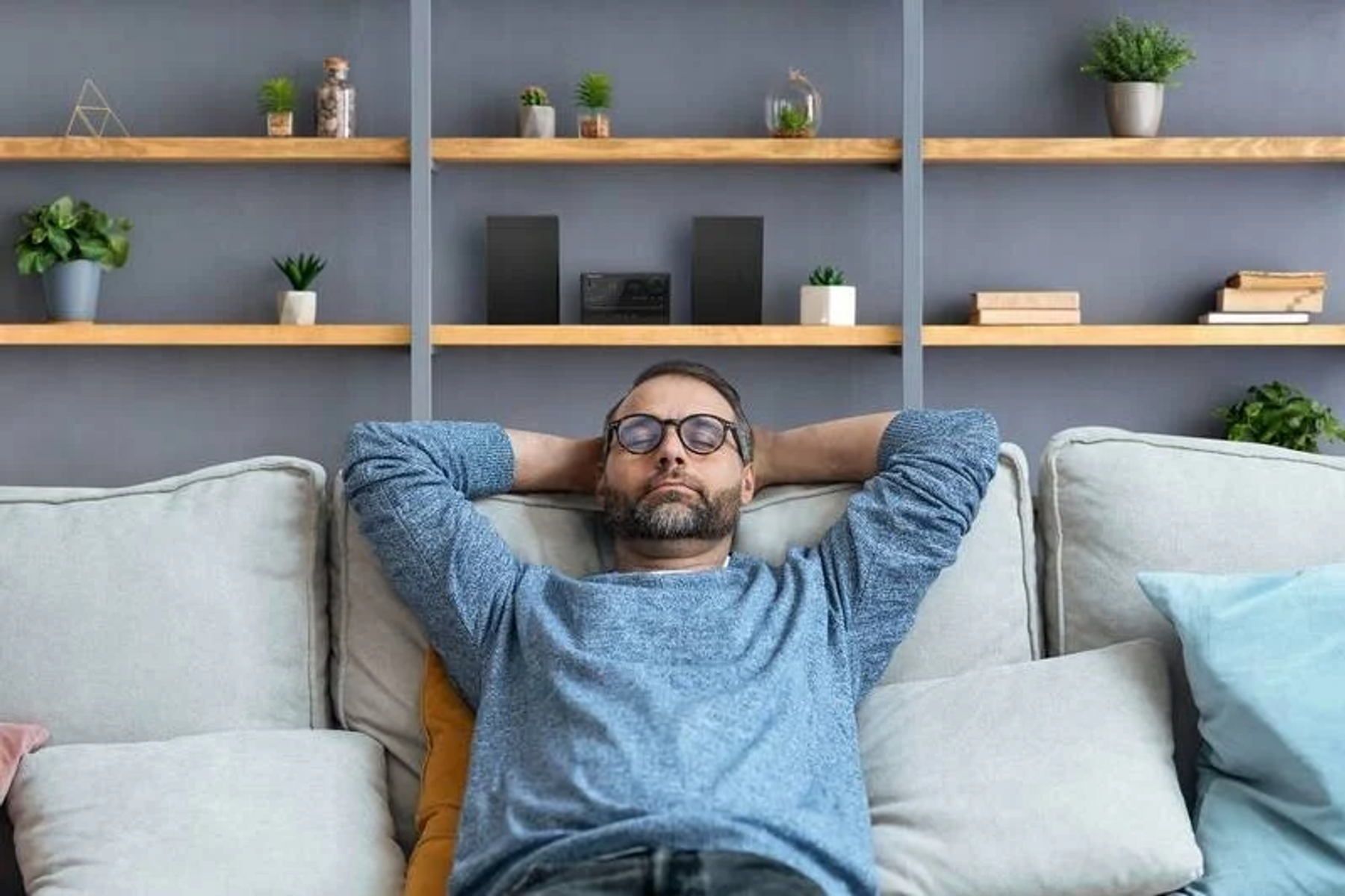 Ein Mann mit Brille auf einem Sofa mit den Händen hinter dem Kopf.