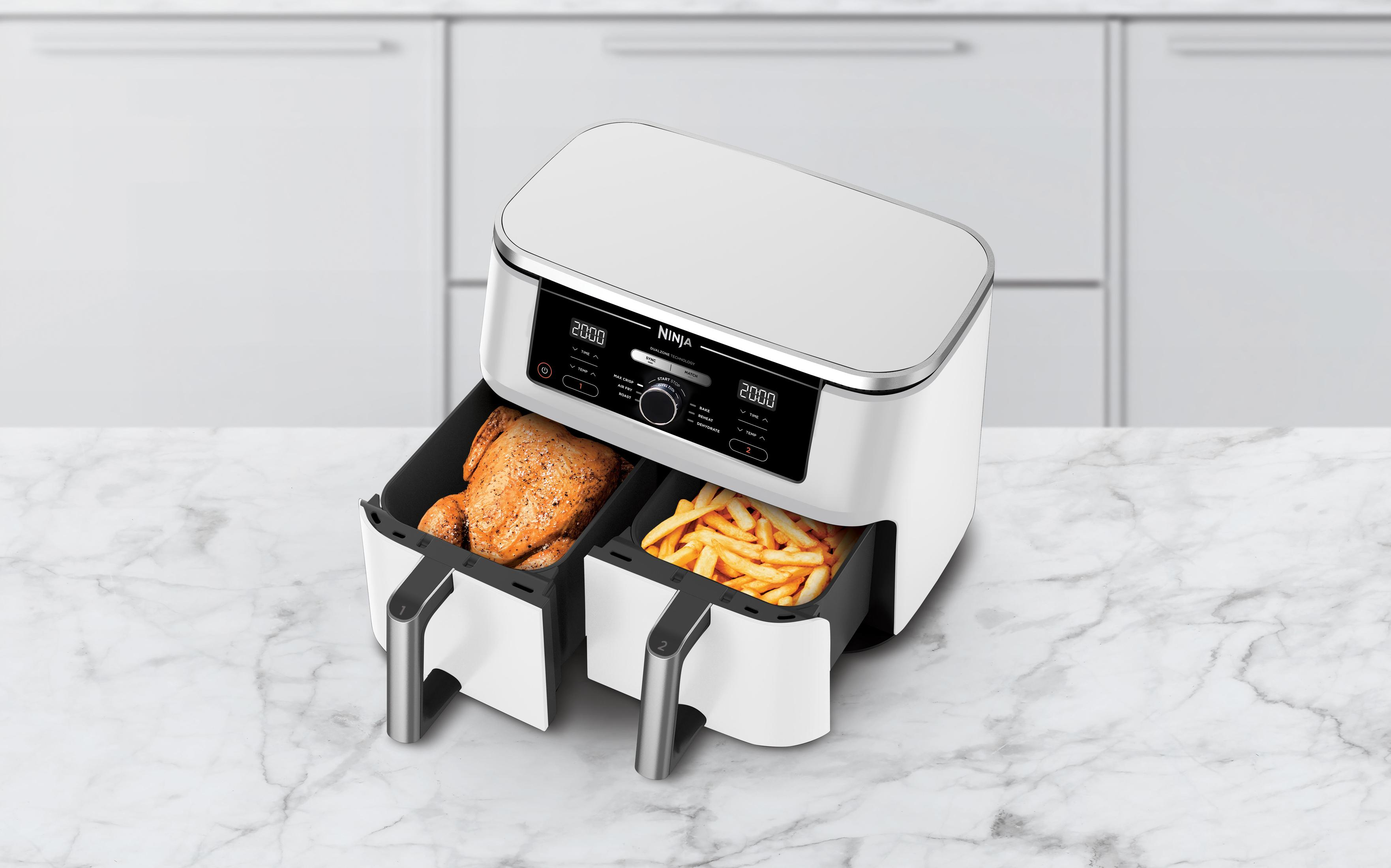 Biała i szara frytkownica powietrzna z jedzeniem w szufladach. Marmurowy blat i biała szafka w tle.