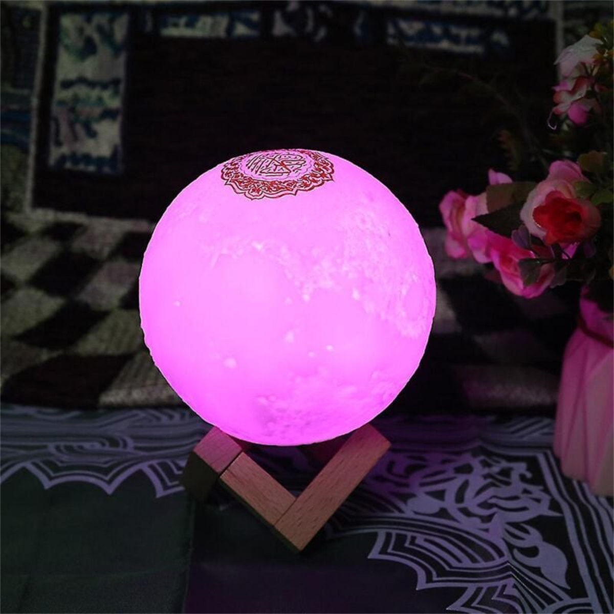 Eine rosa mondförmige Lampe auf einem Holzständer. Der Hintergrund ist ein Teppich und Blumen.