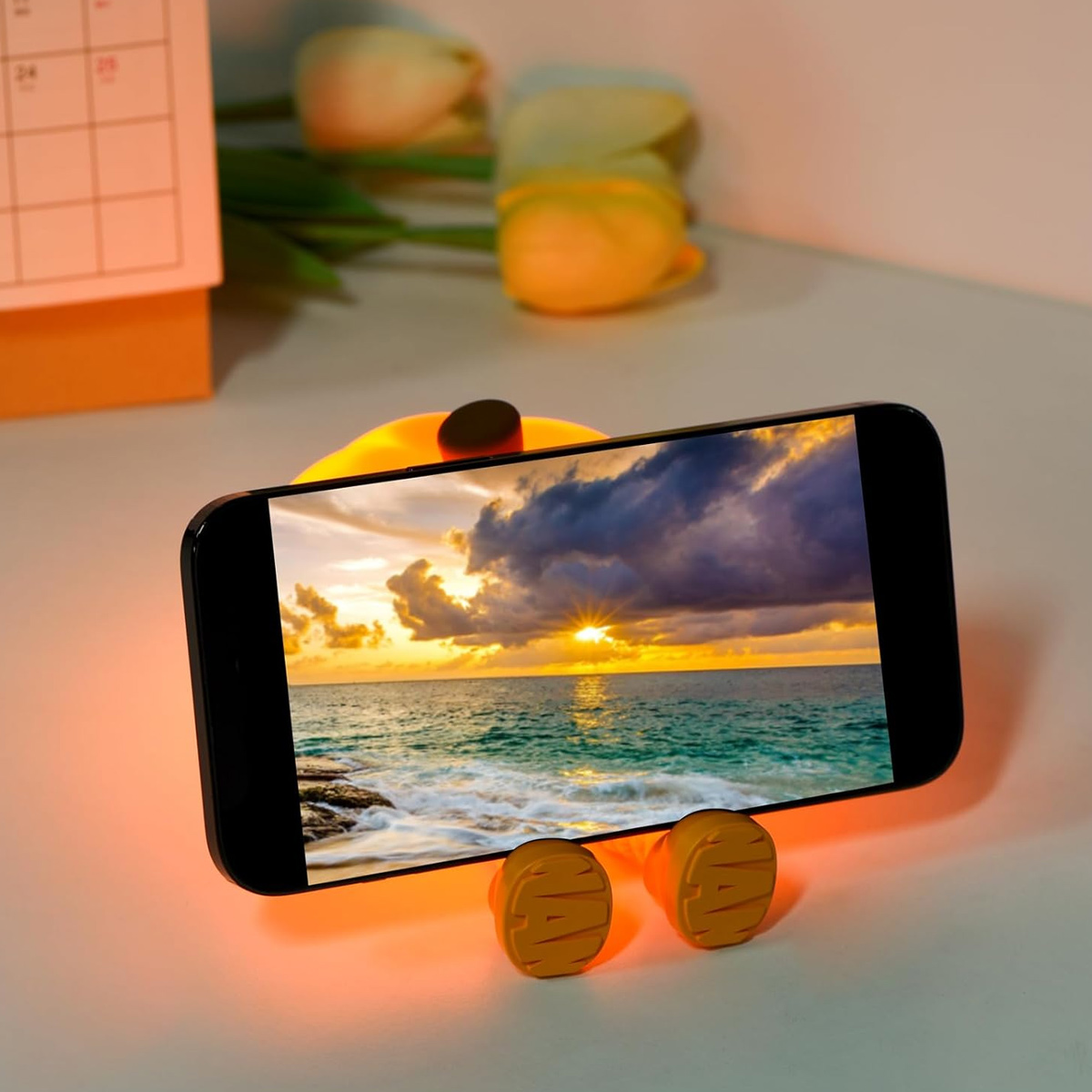 Ein Telefon zeigt einen Sonnenuntergang über dem Meer, das auf einem gelben Enten-Ständer ruht.