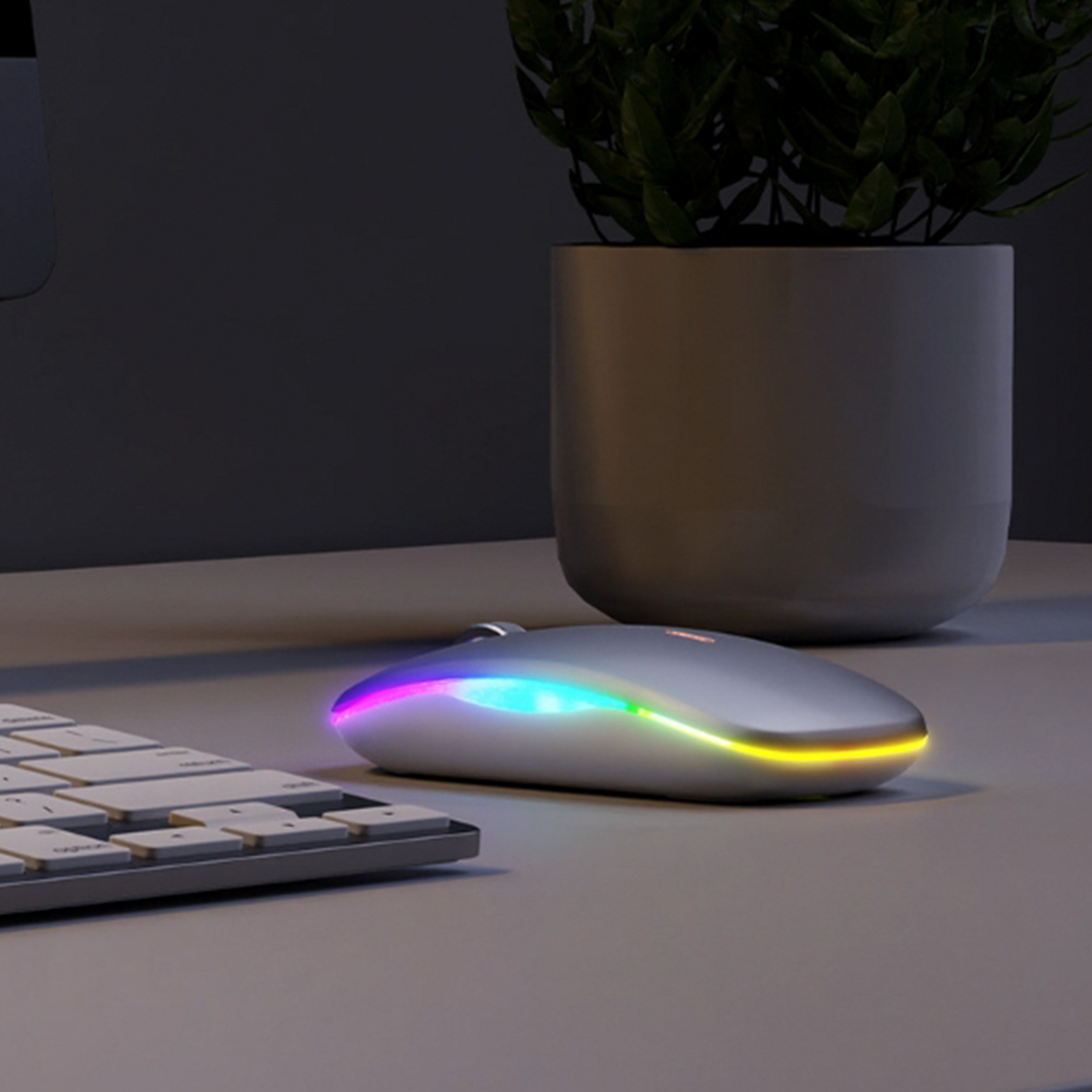 Eine silberne Computermaus mit farbigem Lichtstreifen. Eine Tastatur und eine Pflanze sind im Hintergrund.