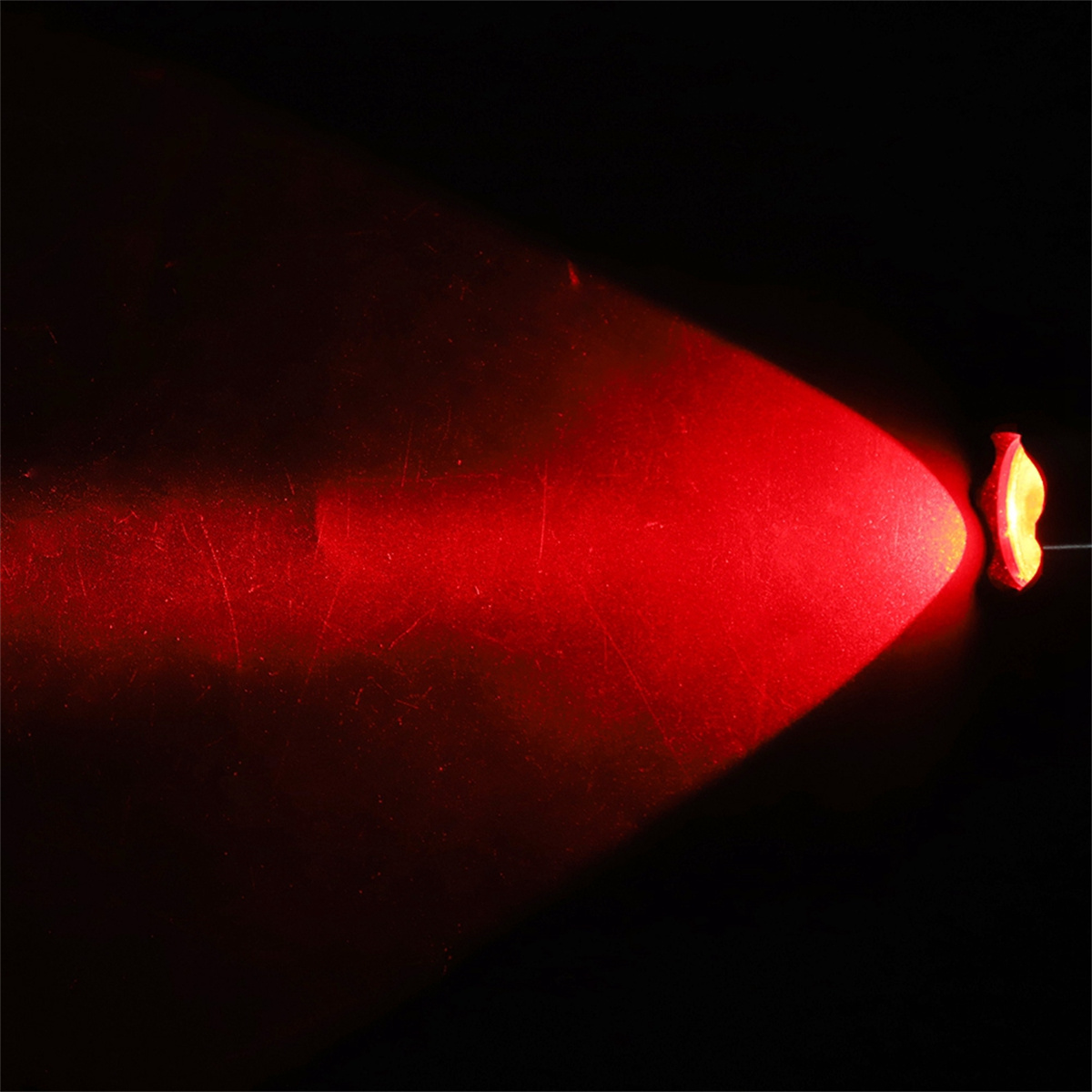 Ein heller roter Lichtstrahl, der von einem kleinen Objekt in dunkler Umgebung scheint.