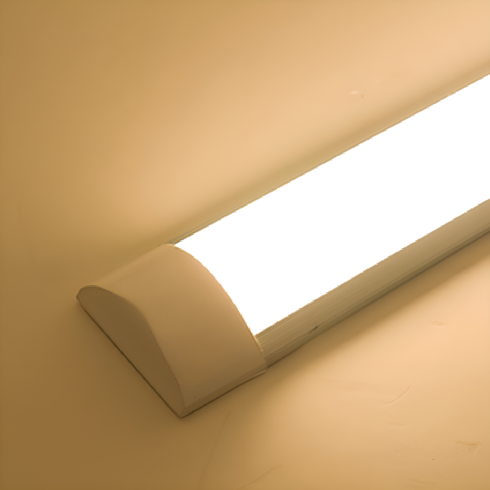 Eine lange, weiße LED-Leuchte ist an einer beigen Wand montiert. Das Licht ist eingeschaltet und leuchtet hell.
