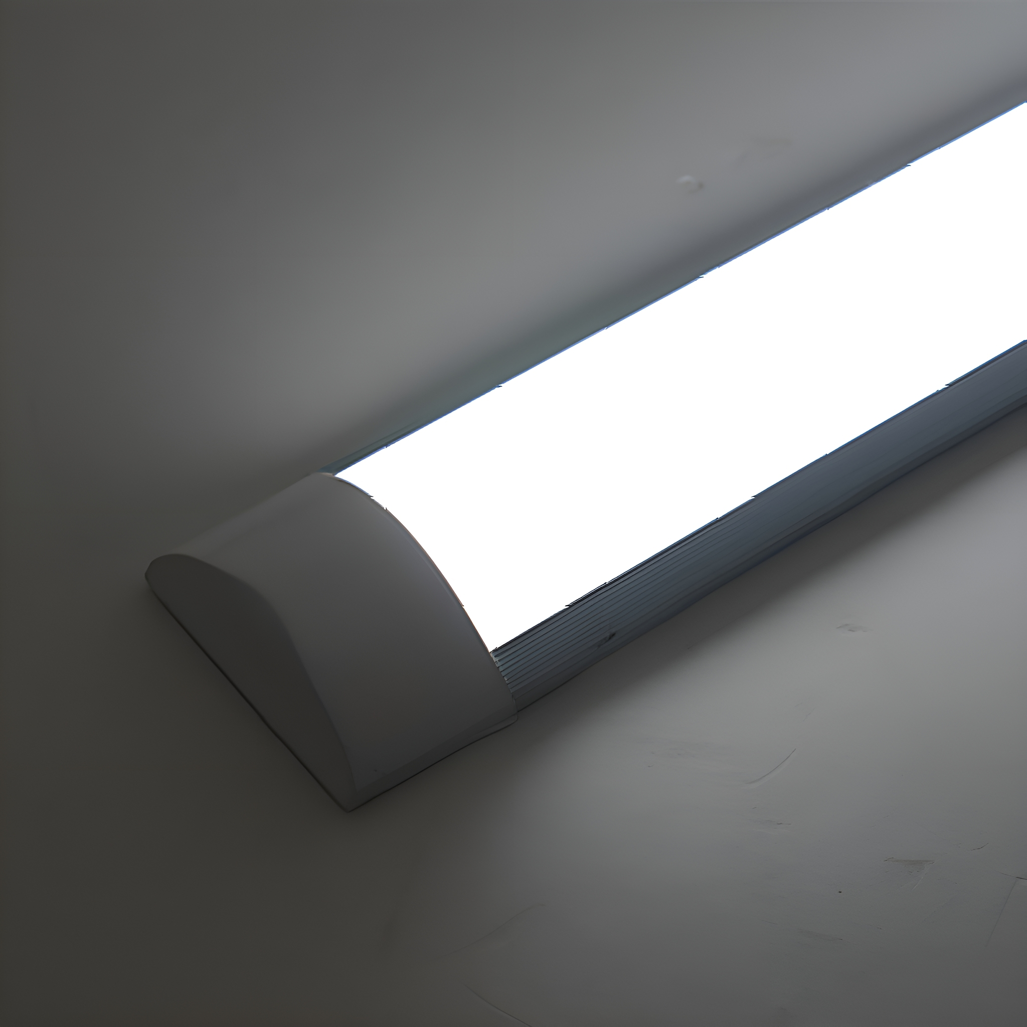 Eine lange, hellweiße LED-Leuchte vor einer hellgrauen Wand. Das Licht ist an.