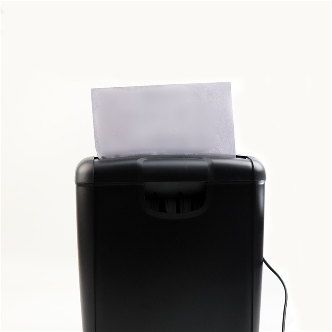 Ein schwarzer Aktenvernichter mit weißem Papier, das hineingezogen wird, vor weißem Hintergrund.