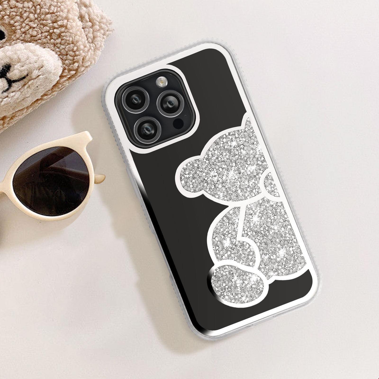 Custodia per telefono nera con un design a orsetto scintillante e occhiali da sole. Sfondo bianco.