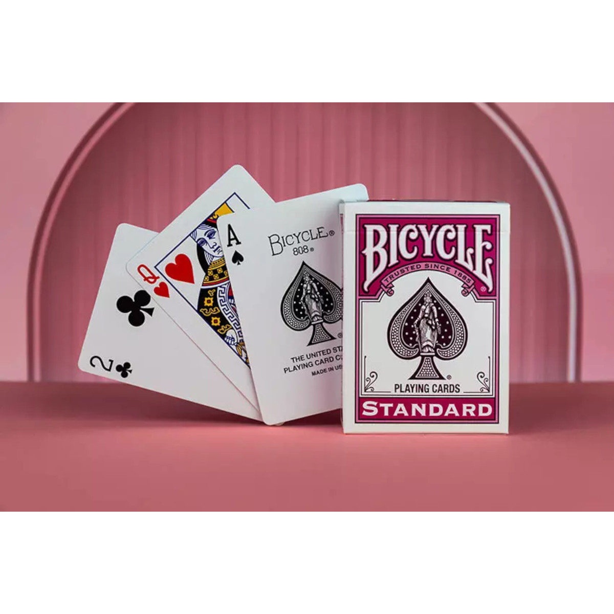 Spielkarten-Deck von Bicycle mit drei aufgefächerten Karten. Die Szene ist auf einer rosa Oberfläche aufgebaut.