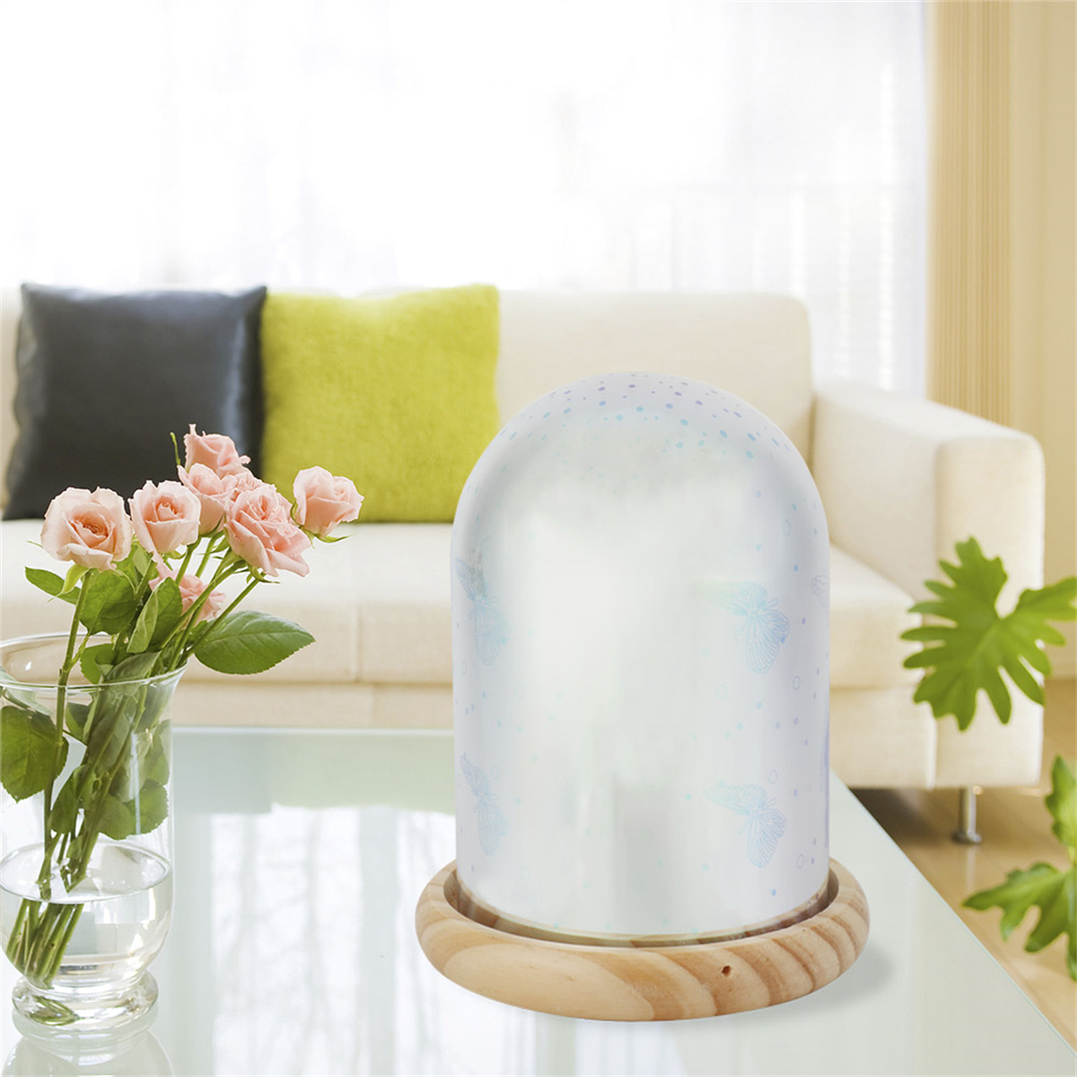 Eine Lampe mit Schmetterlingen, eine Vase mit rosa Rosen und ein weißes Sofa im Hintergrund.