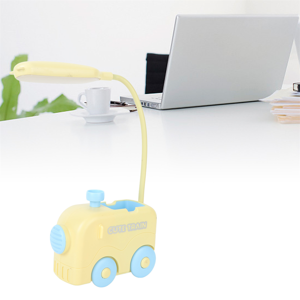Eine gelbe, zugförmige Schreibtischlampe mit Laptop und Tasse auf dem Tisch.
