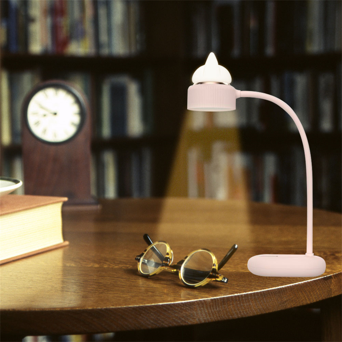 Rosa Schreibtischlampe mit gebogenem Hals, Brille und Buch auf einem Holztisch, Bibliotheks-Hintergrund.