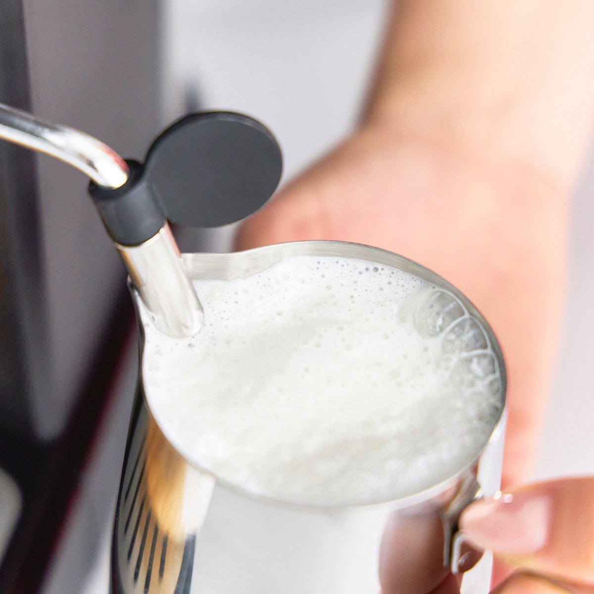 Latte fumante che viene montato in un bricco di acciaio inossidabile da una macchina da caffè.