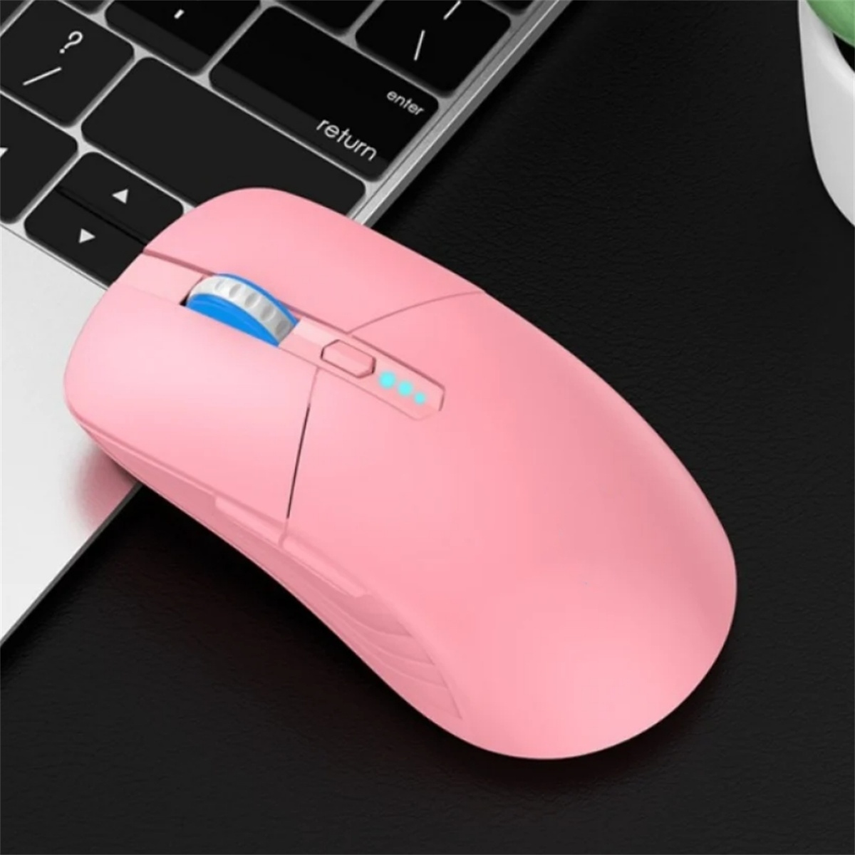 Rosa kabellose Maus auf schwarzer Oberfläche, in der Nähe einer Laptop-Tastatur.