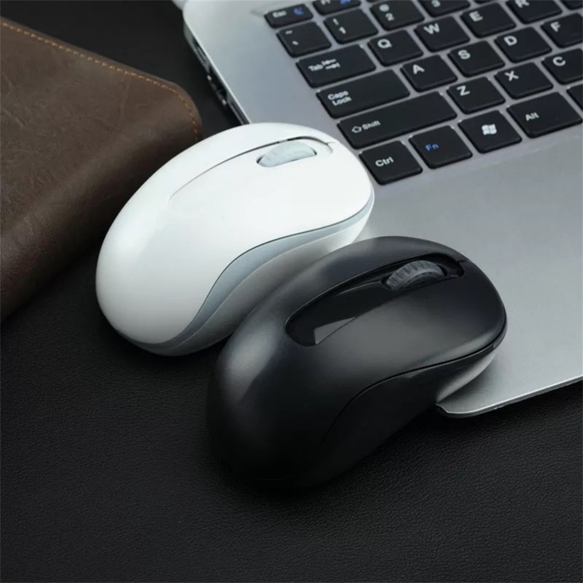 Zwei kabellose Computer-Mäuse. Eine schwarz, eine weiß. Beide auf einer Laptop-Tastatur.