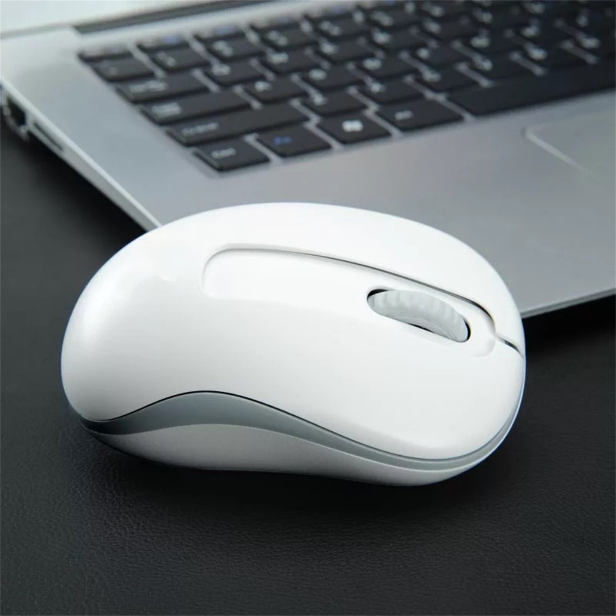 Eine weiße drahtlose Maus neben einer Laptop-Tastatur auf schwarzem Untergrund.