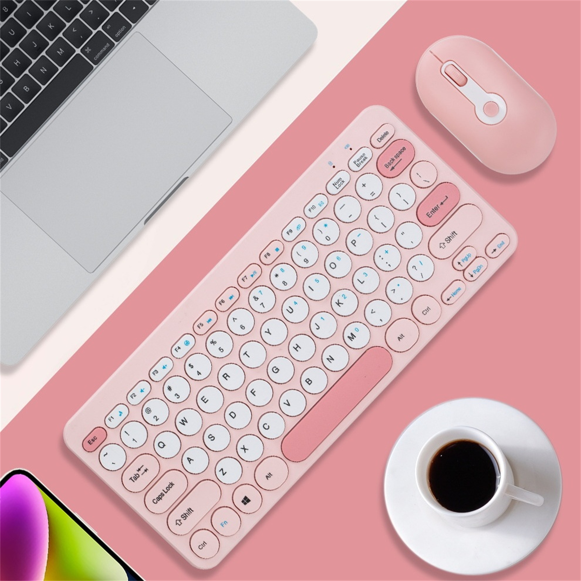 Rosa kabellose Tastatur, Maus und eine Tasse Kaffee auf rosa Oberfläche. Laptop sichtbar.
