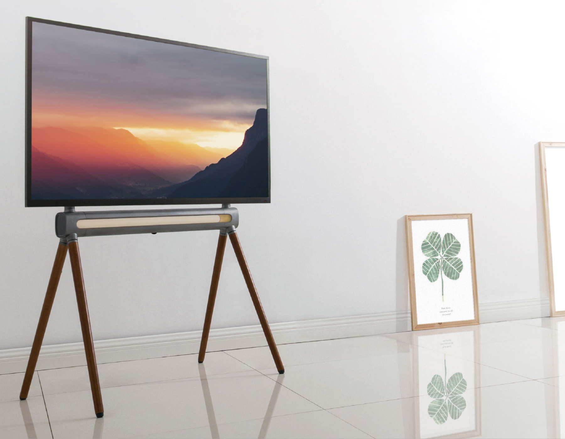 Fernseher auf Holzbeinen, mit Sonnenuntergang. Ein Bilderrahmen mit Klee steht daneben.