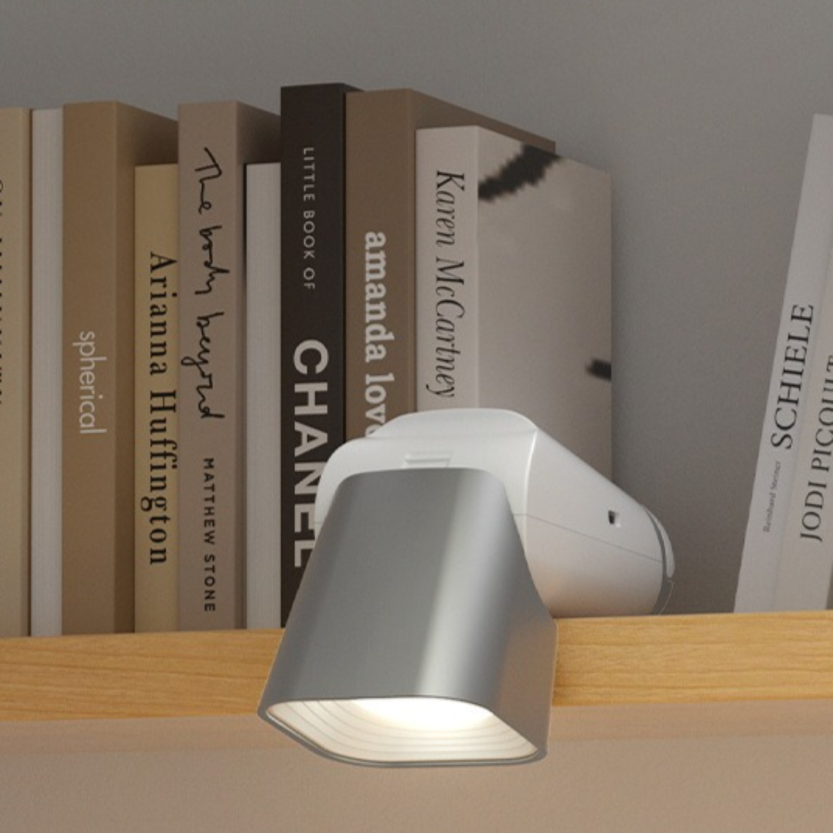 Weiße und silberne Regal-Lampe neben Büchern auf einem Holzregal, das Licht ist an.