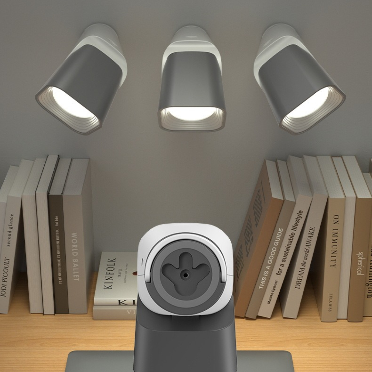 Drei Einbauleuchten über Büchern auf einem Holzschreibtisch und einer Schreibtischlampe.