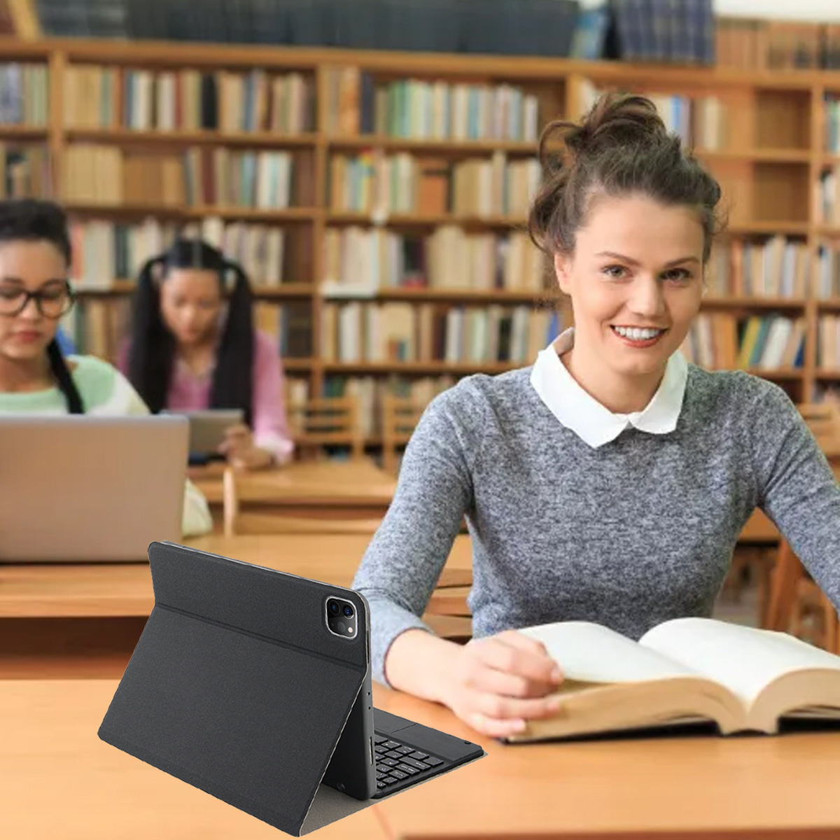 Frau liest lächelnd ein Buch in der Bibliothek. Ein iPad mit Tastatur liegt auf dem Tisch.