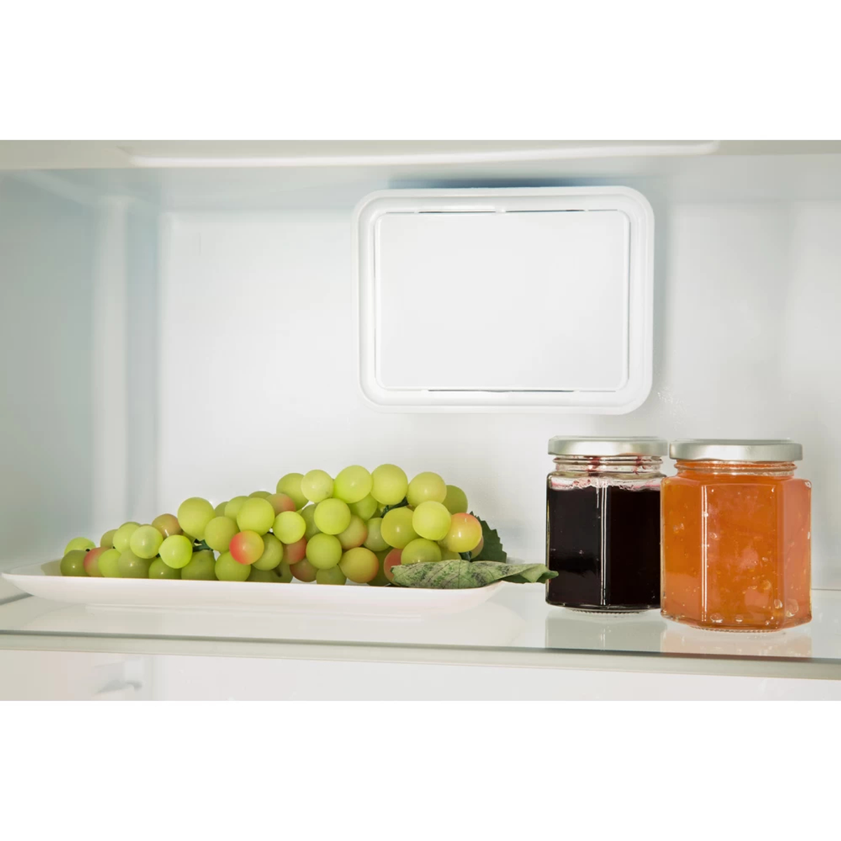 Estante de nevera con uvas, dos frascos de mermelada y una caja blanca.