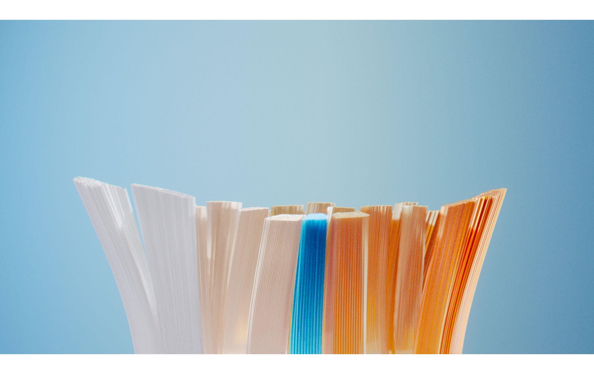 Zbliżenie na główkę szczoteczki do zębów z mieszanym włosiem: białym, beżowym, niebieskim i pomarańczowym, na jasnoniebieskim tle.