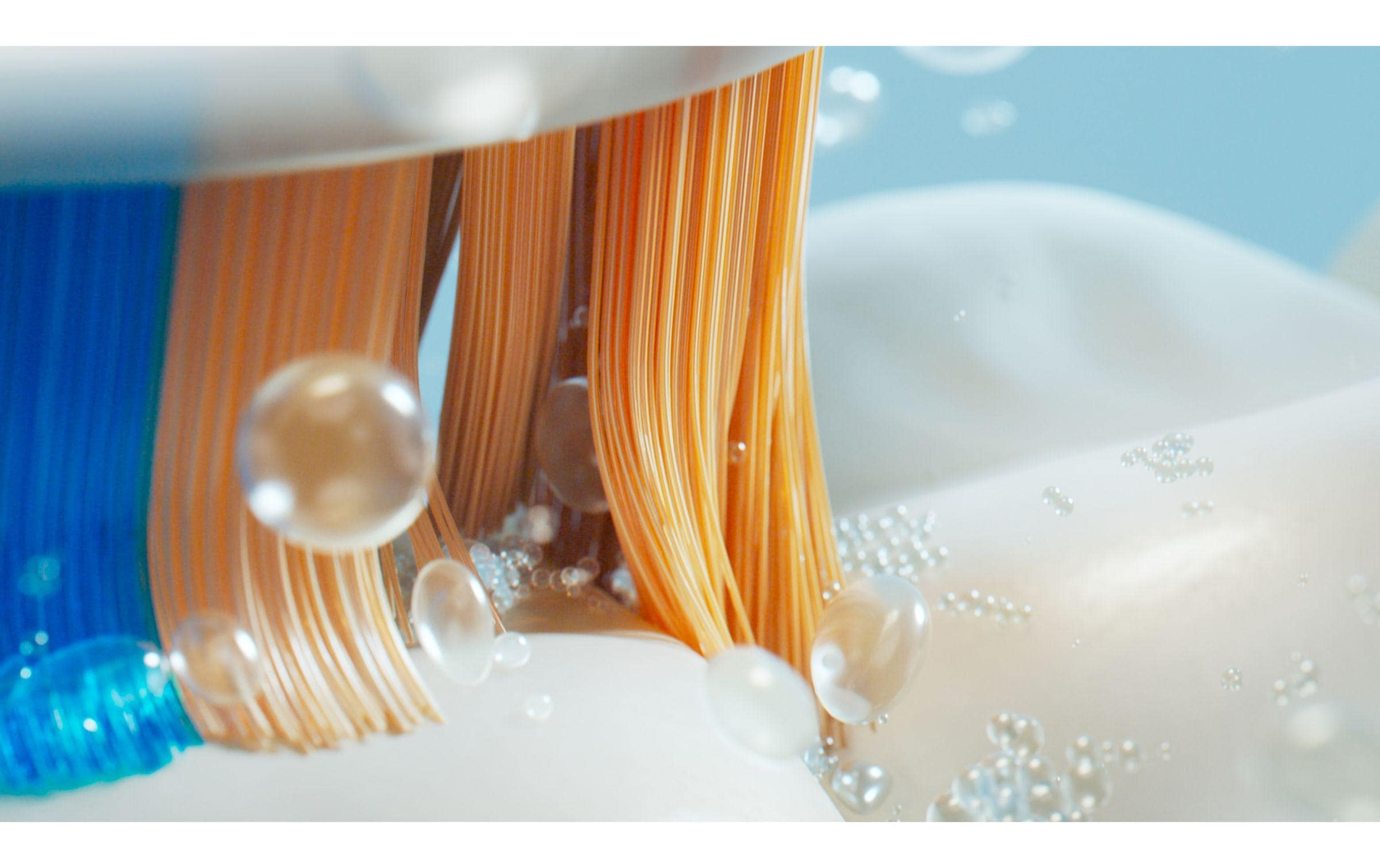 Zbliżenie na włosie szczoteczki do zębów z bąbelkami, pokazujące pomarańczowe włosie.