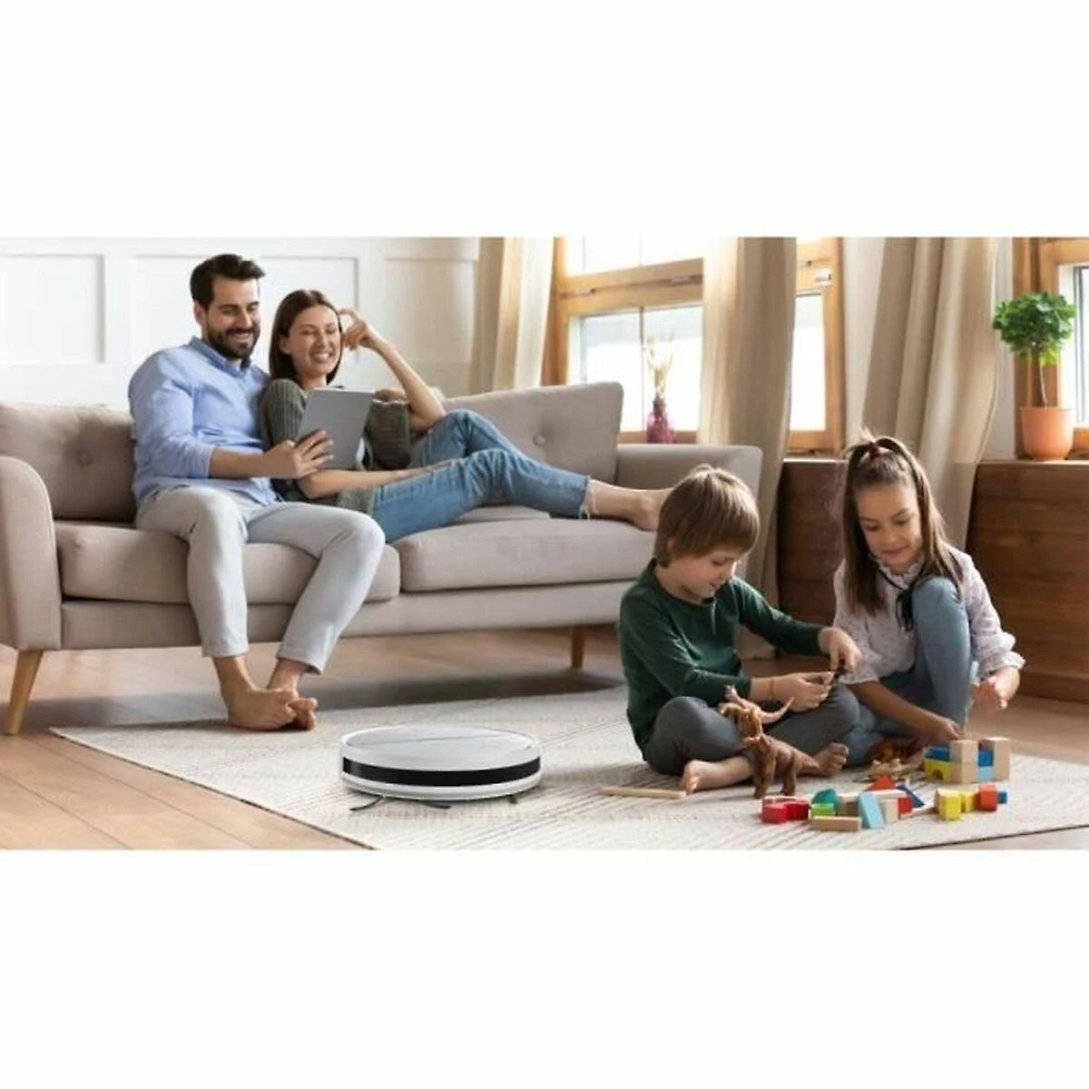 Rodzina na kanapie, korzystająca z tabletu i bawiąca się zabawkami na podłodze. Robot sprząta podłogę.
