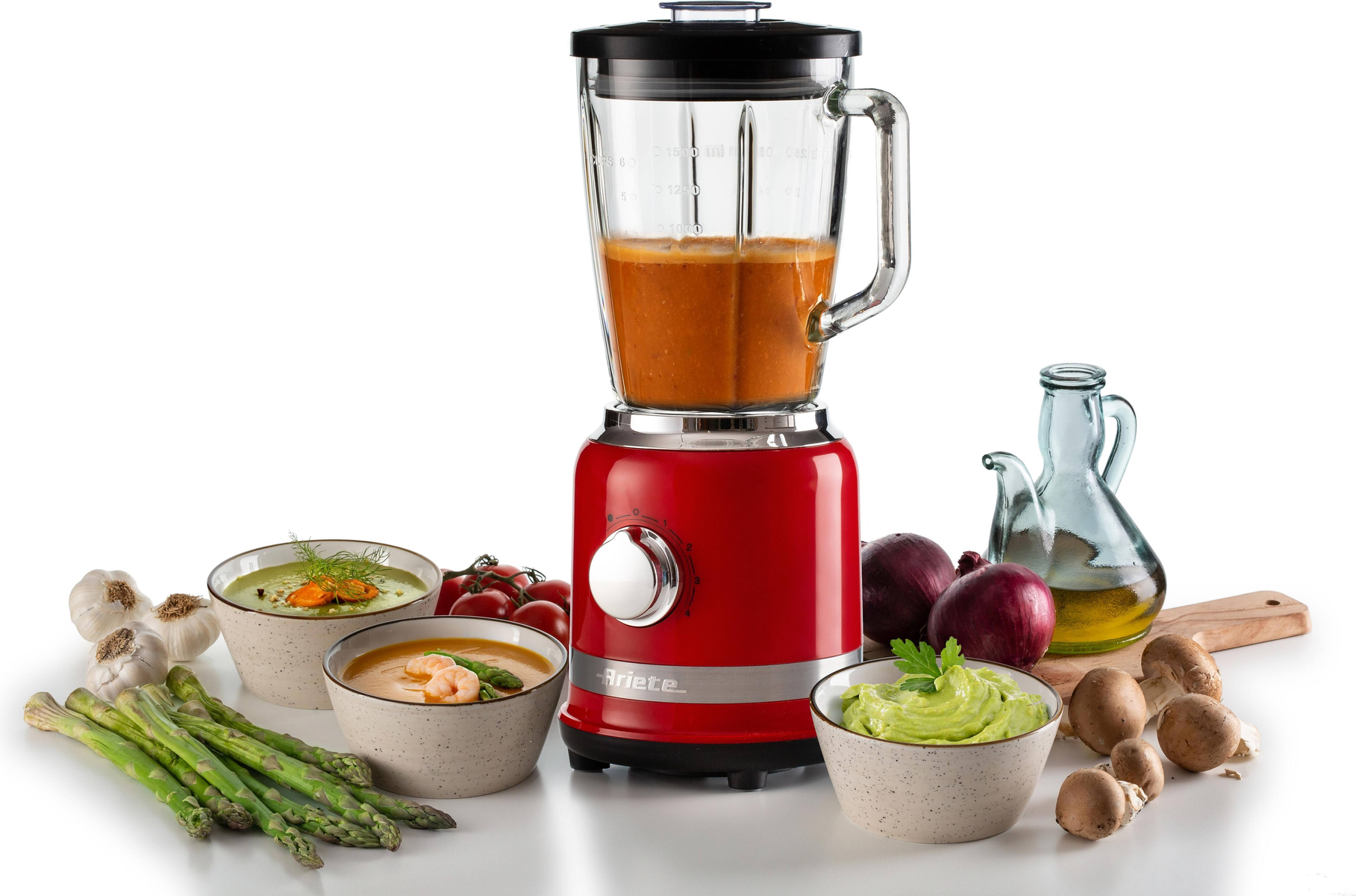 Roter Mixer mit Suppe, Gemüse und Schüsseln mit Essen auf weißer Oberfläche.