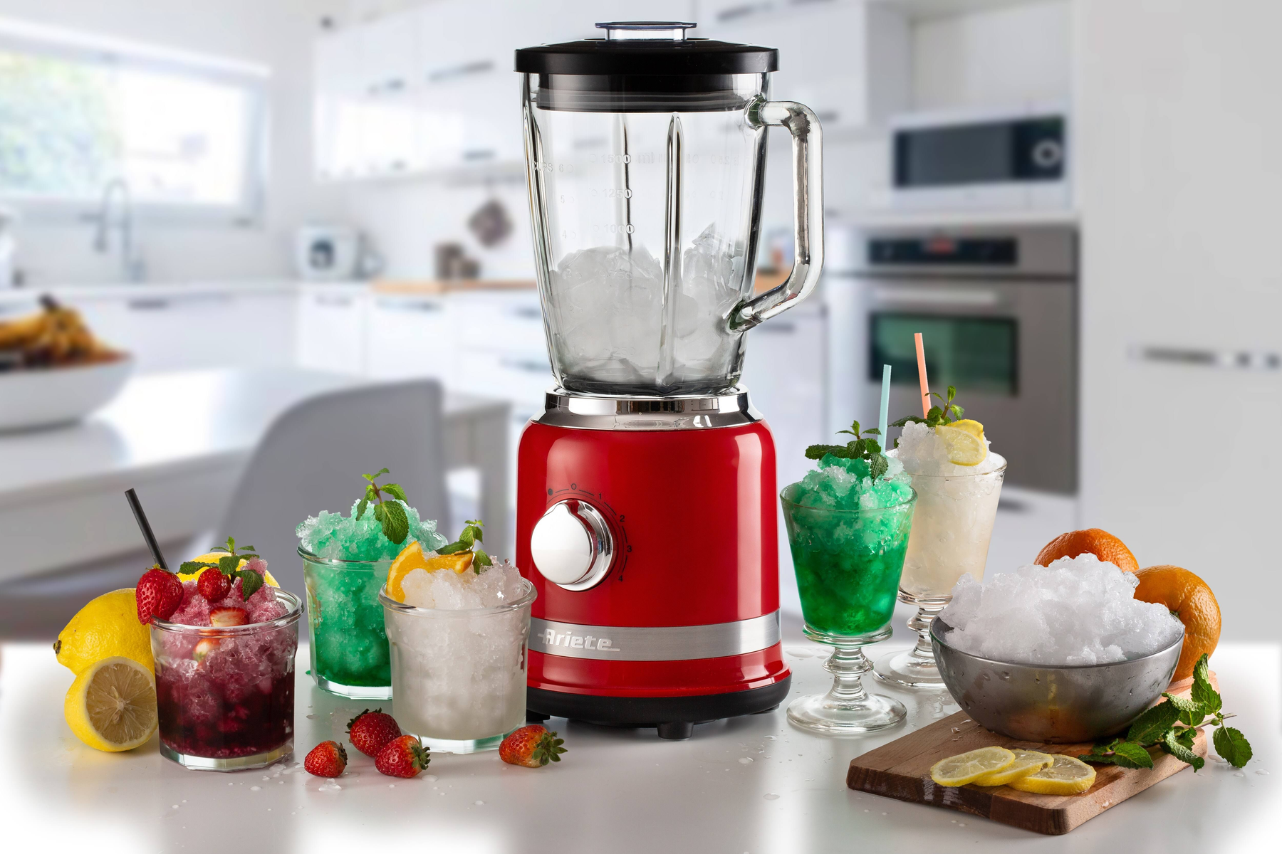Ein roter Mixer mit Eis und Getränken. Gläser mit grünen und weißen Getränken, Eis und Früchten stehen auf einer Theke.