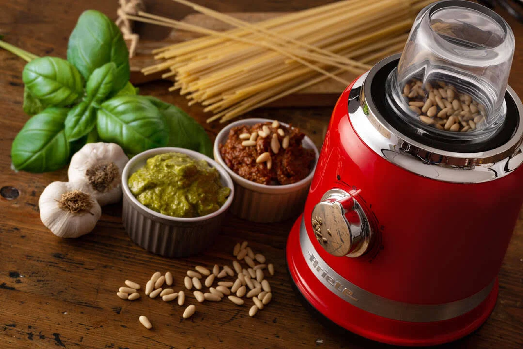 Roter Mixer mit Pesto, Soße, Basilikum, Knoblauch und Pinienkernen auf Holz.
