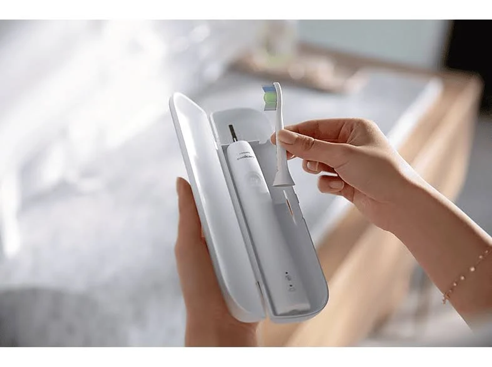 Dłonie trzymają białe etui na szczoteczkę do zębów, zawierające szczoteczkę elektryczną.