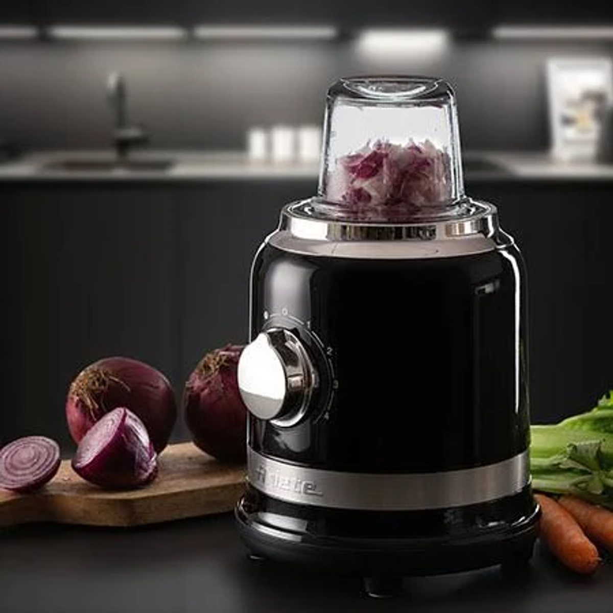 Robot da cucina nero con cipolle rosse, tagliere e altre verdure.