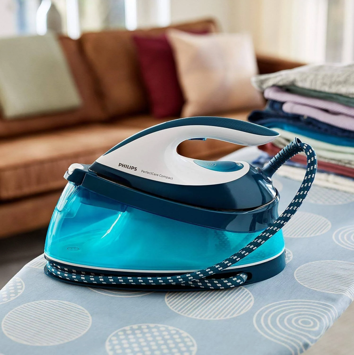 Plancha de vapor Philips sobre tabla de planchar, con pila de ropa detrás.