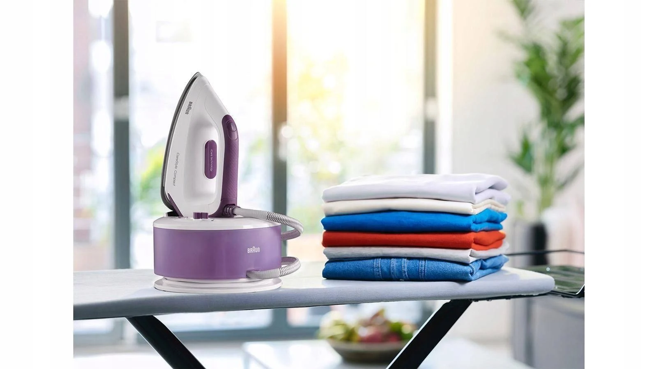Bügelbrett mit Bügeleisen und gefalteter Kleidung. Bügeleisen ist weiß und lila.